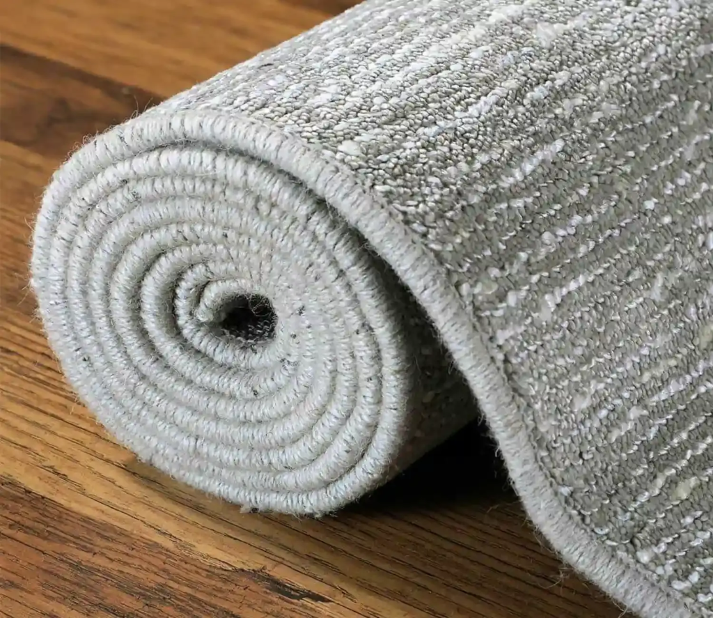 light grey textured carpet rolled neatly on a wooden floor, showing its woven pattern and thickness